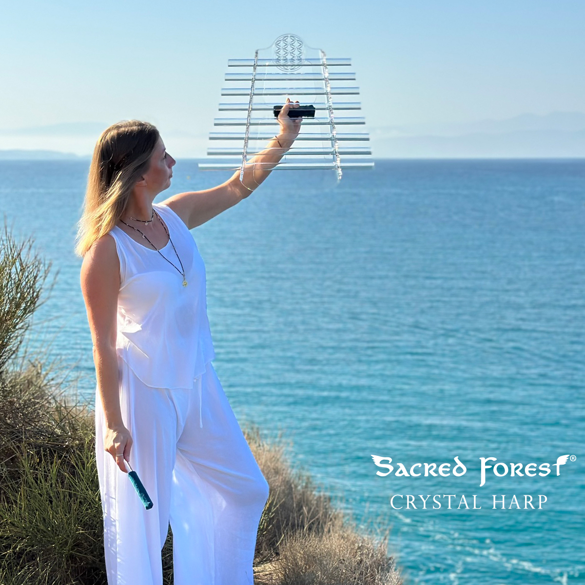 Natalia standing with Sacred Forest Crystal Harp at beautiful, stuning, turquoise seashore